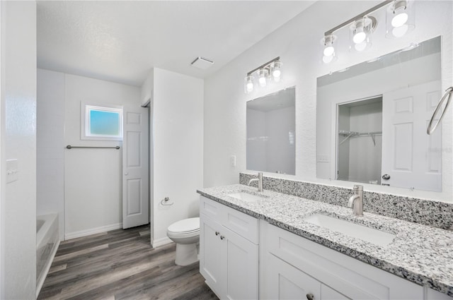 bathroom featuring double vanity, wood finished floors, a sink, and toilet