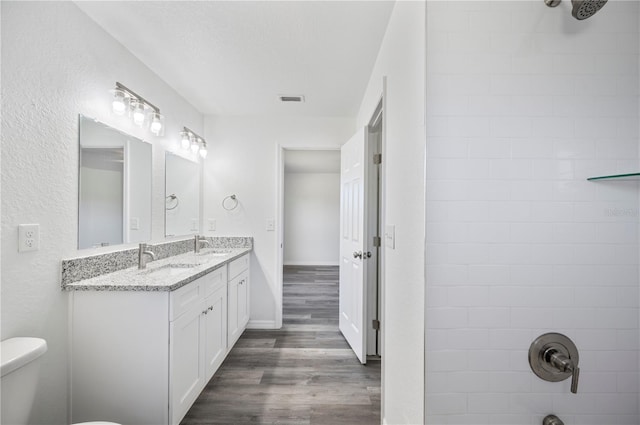 full bath with double vanity, visible vents, a sink, and wood finished floors