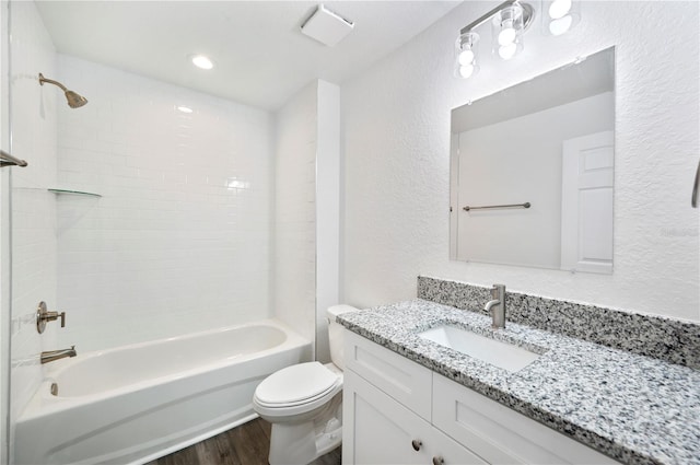 full bath featuring a textured wall, toilet, wood finished floors, vanity, and washtub / shower combination