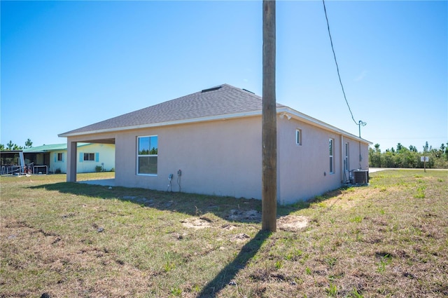 rear view of property with roof with shingles, central AC, a lawn, and stucco siding