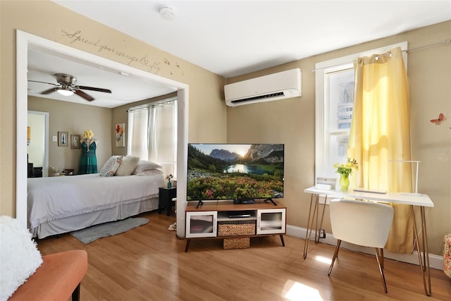 bedroom with a wall mounted air conditioner, hardwood / wood-style flooring, and ceiling fan