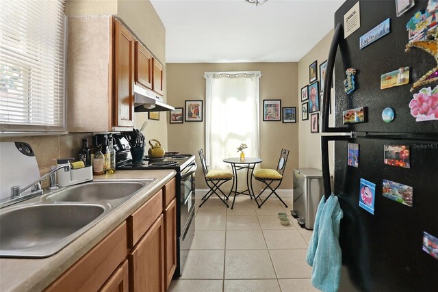 kitchen with black refrigerator, light tile patterned floors, stainless steel range, and sink