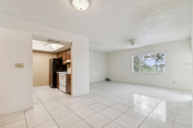 unfurnished living room featuring a textured ceiling, a skylight, ceiling fan, and light tile patterned flooring