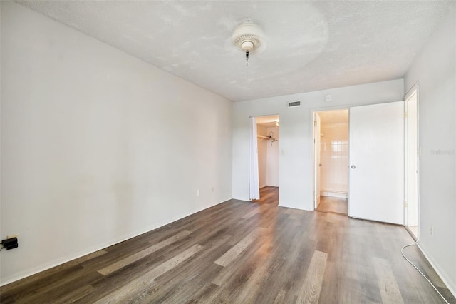 unfurnished bedroom featuring connected bathroom, a textured ceiling, a walk in closet, a closet, and hardwood / wood-style flooring