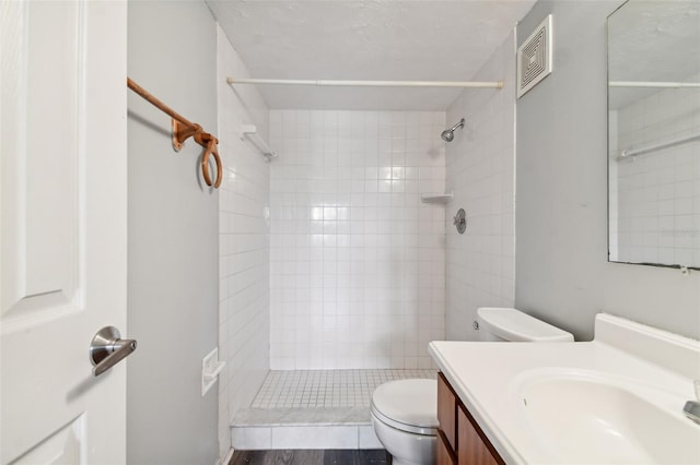 bathroom with tiled shower, hardwood / wood-style floors, vanity, and toilet