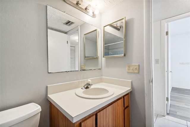 bathroom featuring tile patterned flooring, a textured ceiling, vanity, and toilet