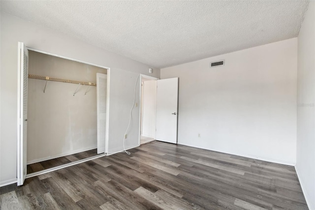 unfurnished bedroom featuring a textured ceiling, a closet, and dark wood-type flooring