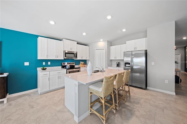 kitchen with a kitchen bar, appliances with stainless steel finishes, light stone counters, a kitchen island with sink, and white cabinets