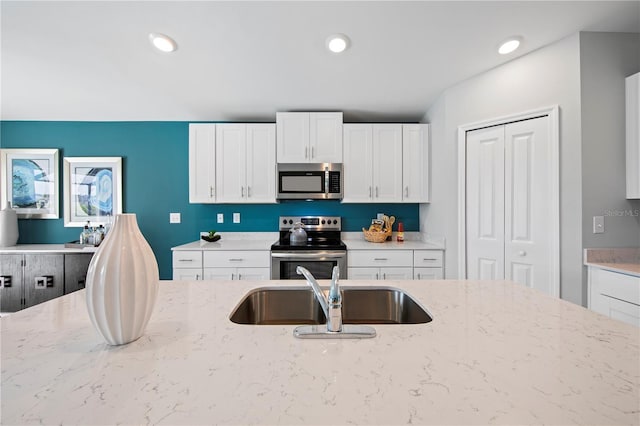 kitchen with appliances with stainless steel finishes, white cabinetry, light stone counters, and sink