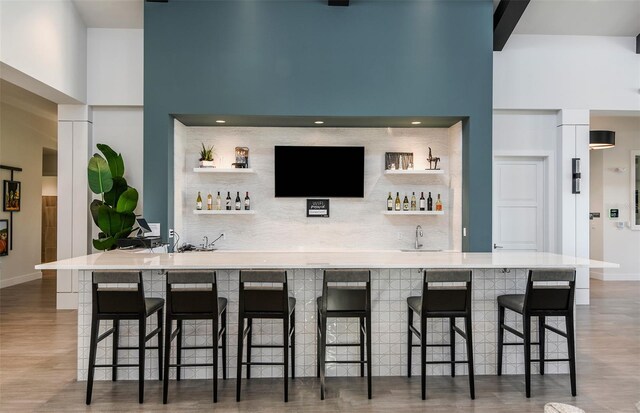 bar with a towering ceiling, tasteful backsplash, and dark hardwood / wood-style flooring