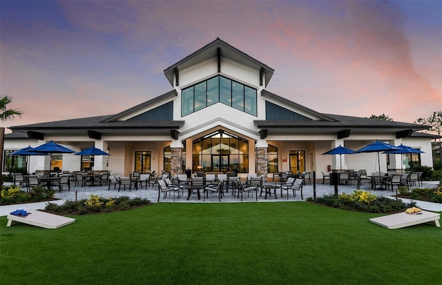 back house at dusk with a patio and a lawn