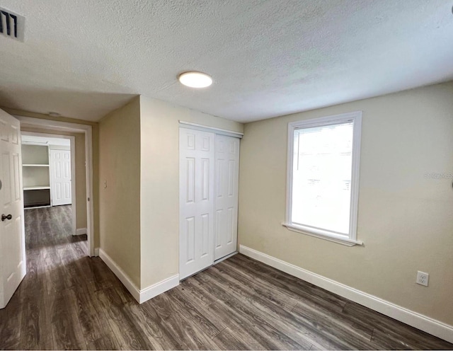 unfurnished bedroom featuring a textured ceiling, dark hardwood / wood-style flooring, and a closet