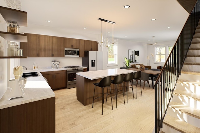 kitchen featuring light wood-type flooring, sink, pendant lighting, appliances with stainless steel finishes, and a kitchen breakfast bar