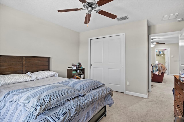 bedroom with ceiling fan, a closet, light carpet, and a textured ceiling