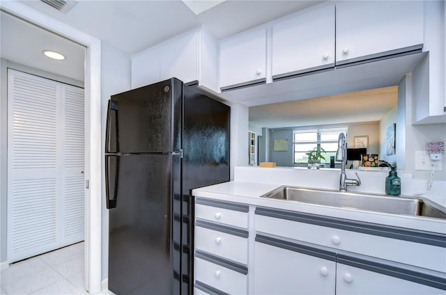 kitchen with white cabinets, light tile patterned floors, black fridge, and sink