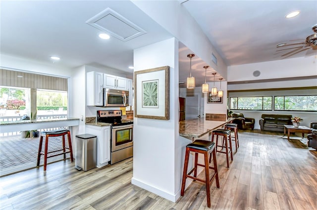 kitchen with appliances with stainless steel finishes, light wood-type flooring, pendant lighting, white cabinetry, and a breakfast bar area