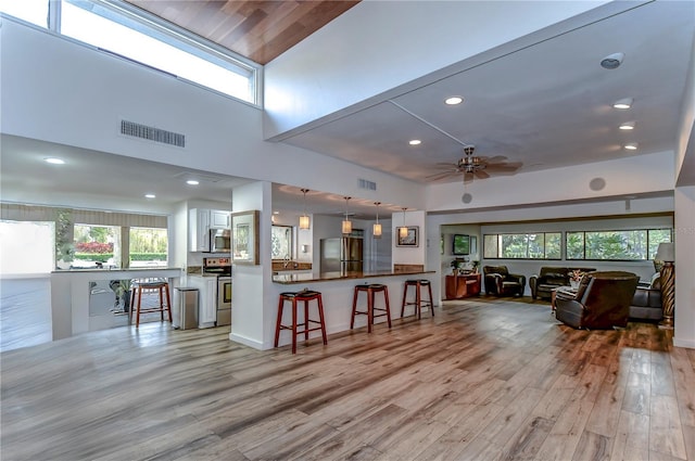 living room with a high ceiling, light wood-type flooring, and ceiling fan