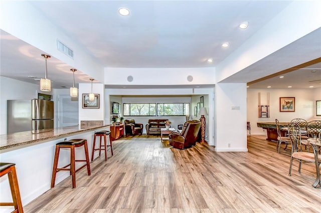 kitchen featuring light stone countertops, stainless steel fridge, a breakfast bar, pendant lighting, and light hardwood / wood-style floors