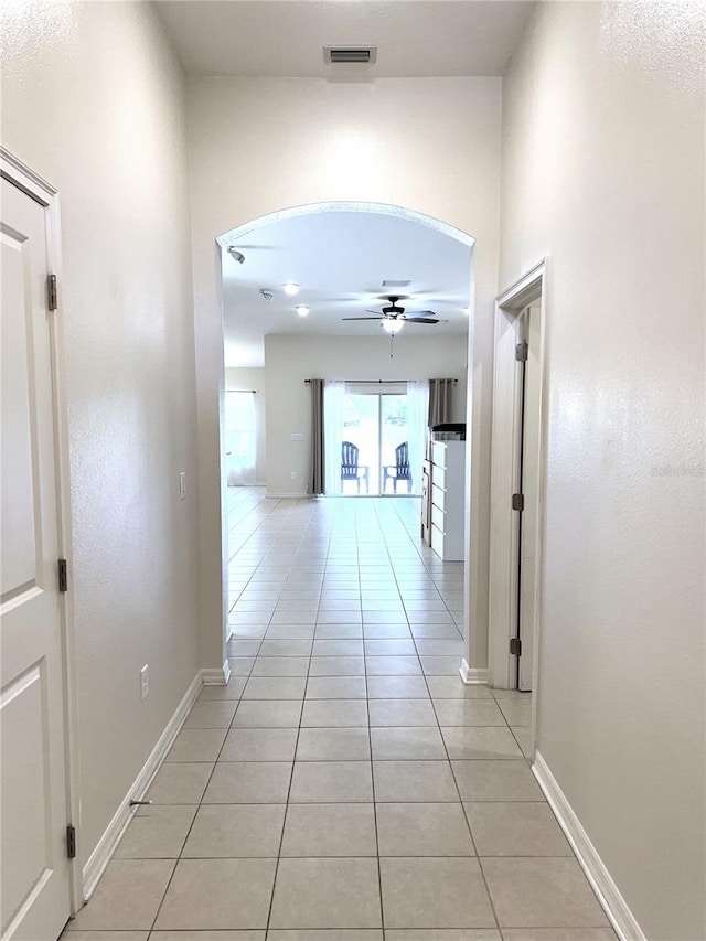 corridor featuring arched walkways, visible vents, baseboards, and light tile patterned flooring