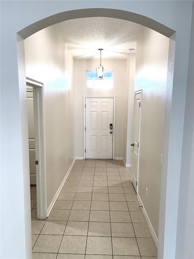 doorway to outside with light tile patterned floors, arched walkways, a textured ceiling, and baseboards