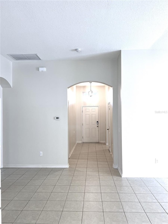 hall featuring baseboards, visible vents, light tile patterned flooring, arched walkways, and a textured ceiling