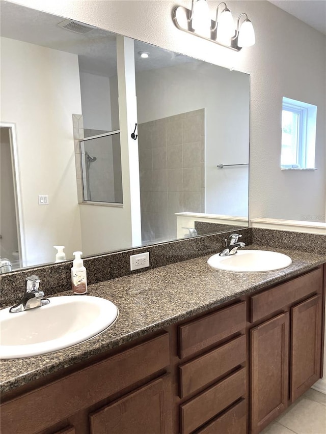 full bath featuring a tile shower, visible vents, double vanity, and a sink