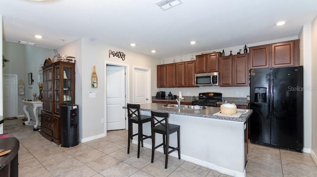 kitchen with a kitchen breakfast bar, a kitchen island with sink, sink, black appliances, and light tile patterned floors