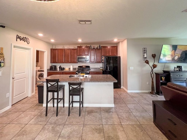 kitchen with black appliances, a center island with sink, light tile patterned floors, a kitchen bar, and washer / clothes dryer