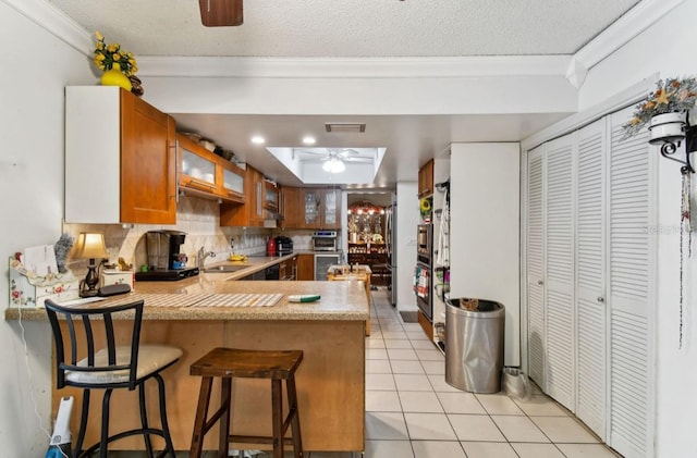 kitchen with ceiling fan, sink, kitchen peninsula, crown molding, and light tile patterned flooring