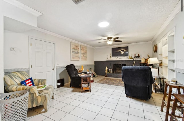 living room with a brick fireplace, ceiling fan, ornamental molding, a textured ceiling, and light tile patterned floors