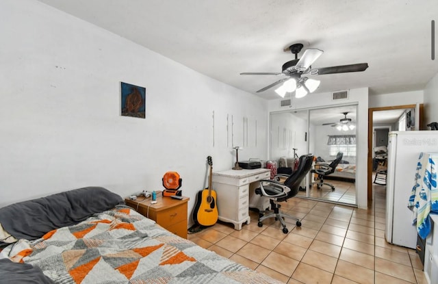 bedroom featuring ceiling fan, white fridge, light tile patterned floors, and a closet