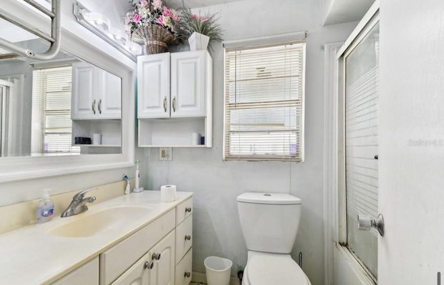 full bathroom with toilet, vanity, a healthy amount of sunlight, and combined bath / shower with glass door