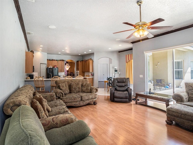 living room with a textured ceiling, light wood-type flooring, and ceiling fan