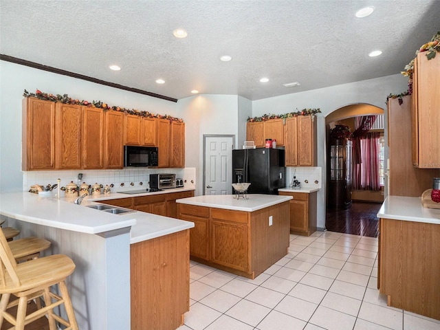 kitchen with black appliances, sink, light tile patterned floors, a kitchen bar, and kitchen peninsula