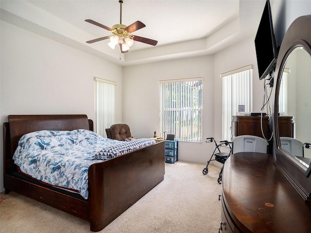 carpeted bedroom with a raised ceiling and ceiling fan