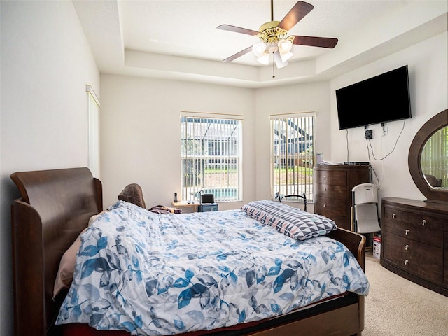 bedroom featuring ceiling fan, light carpet, and a tray ceiling