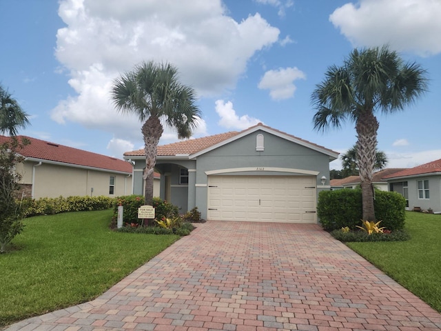 view of front of house featuring an attached garage, a tiled roof, decorative driveway, stucco siding, and a front lawn