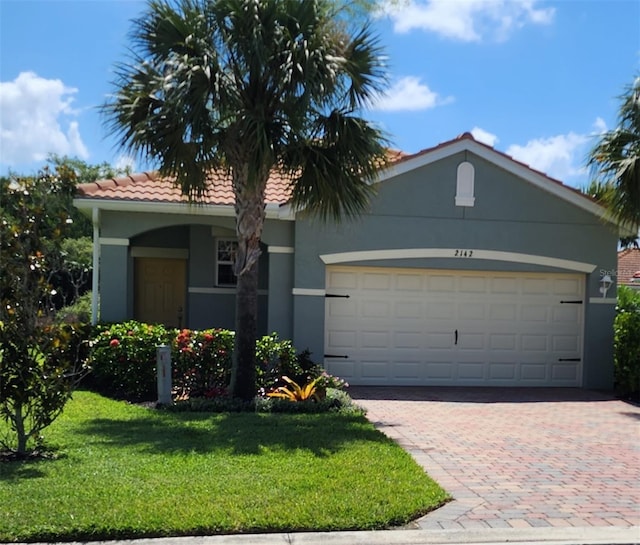 view of front of house with a garage, a tile roof, decorative driveway, stucco siding, and a front yard