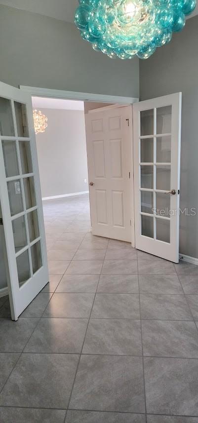 empty room with baseboards, french doors, and tile patterned floors