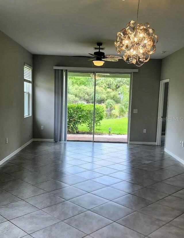 unfurnished room with baseboards, ceiling fan with notable chandelier, light tile patterned flooring, and a healthy amount of sunlight