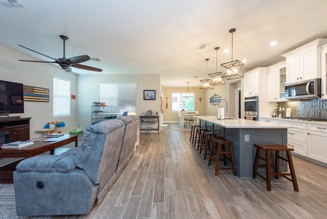 kitchen with a breakfast bar area, ceiling fan, an island with sink, stainless steel appliances, and pendant lighting