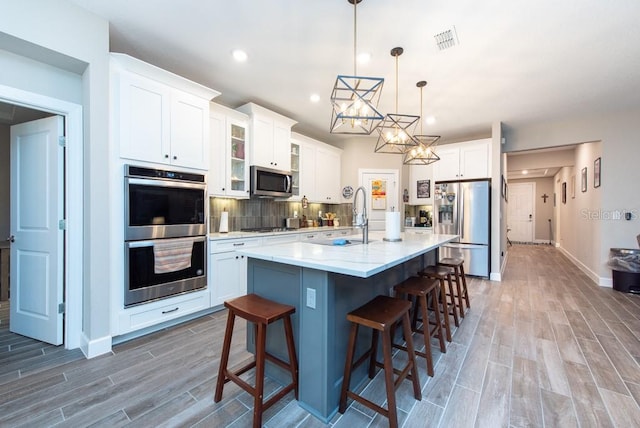 kitchen featuring tasteful backsplash, stainless steel appliances, an island with sink, sink, and a breakfast bar