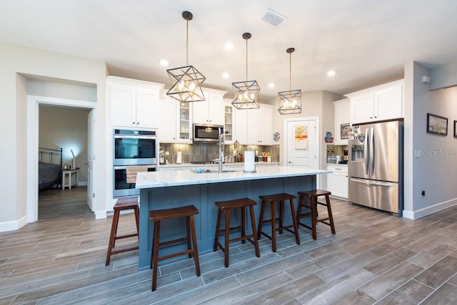 kitchen with appliances with stainless steel finishes, an island with sink, tasteful backsplash, and dark hardwood / wood-style floors