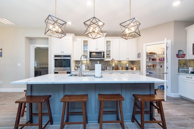 kitchen with white cabinetry, a center island with sink, backsplash, and stainless steel appliances