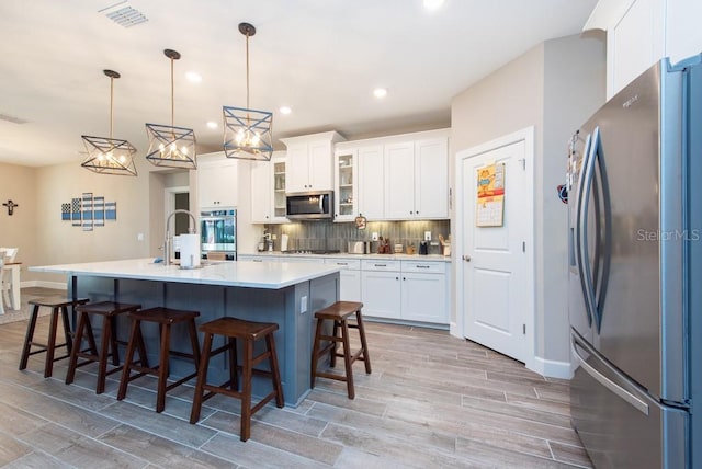 kitchen featuring appliances with stainless steel finishes, white cabinetry, decorative backsplash, and an island with sink