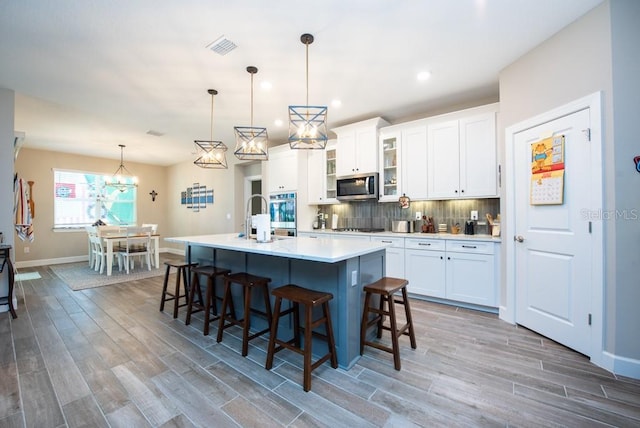 kitchen with stainless steel appliances, backsplash, decorative light fixtures, a kitchen island with sink, and white cabinetry