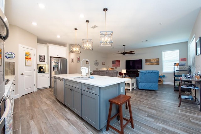 kitchen featuring pendant lighting, white cabinets, light hardwood / wood-style floors, appliances with stainless steel finishes, and a kitchen island with sink