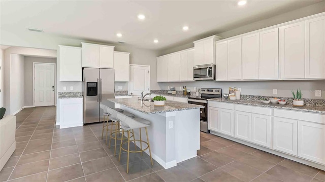 kitchen featuring light stone countertops, a center island with sink, white cabinets, and appliances with stainless steel finishes