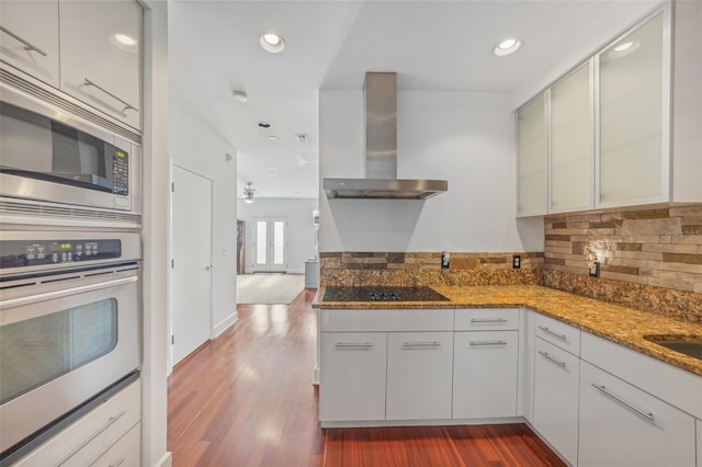 kitchen featuring stone countertops, white cabinets, dark hardwood / wood-style flooring, stainless steel appliances, and wall chimney range hood