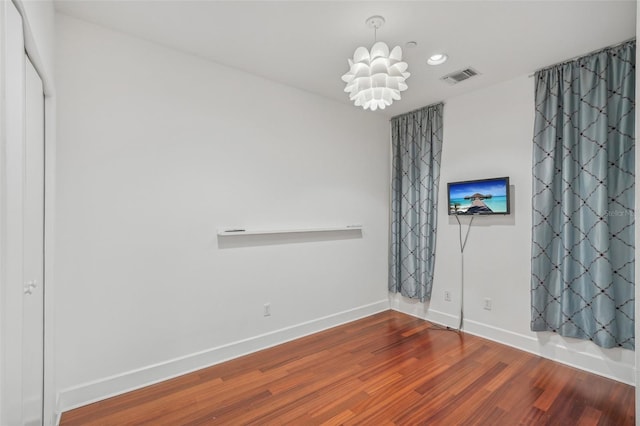 empty room with wood-type flooring and a chandelier